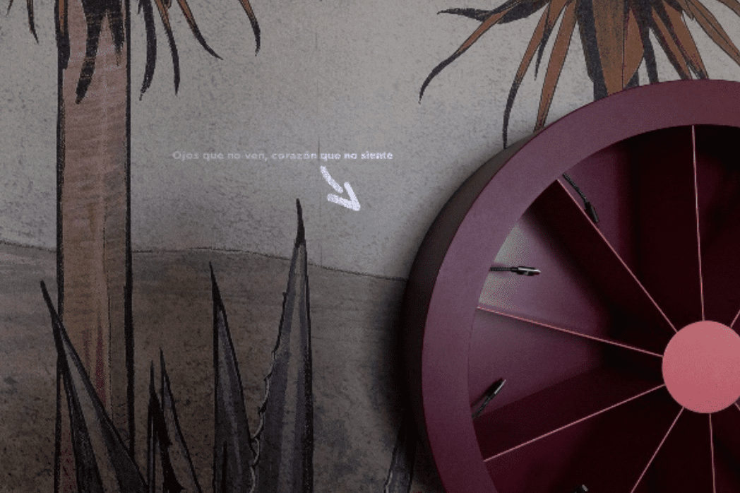 Un détail de décoration murale : une fresque de palmiers et d'agaves, une phrase projetée en espagnol et une grande roue murale bordeaux.