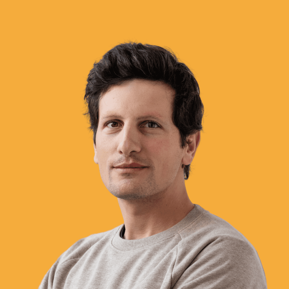Matthieu Nicoletti, met warrig donker haar en een lichte sweater, tegen een gele achtergrond.