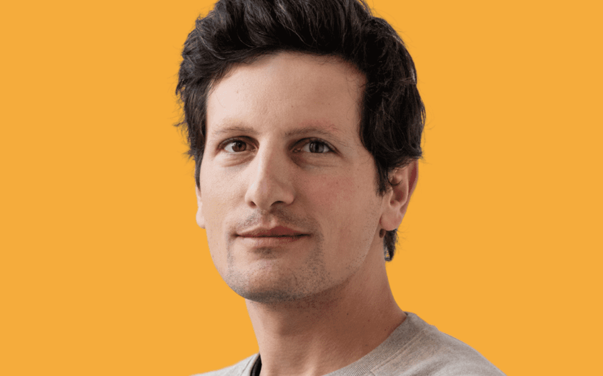 Matthieu Nicoletti, met warrig donker haar en een lichte sweater, tegen een gele achtergrond.