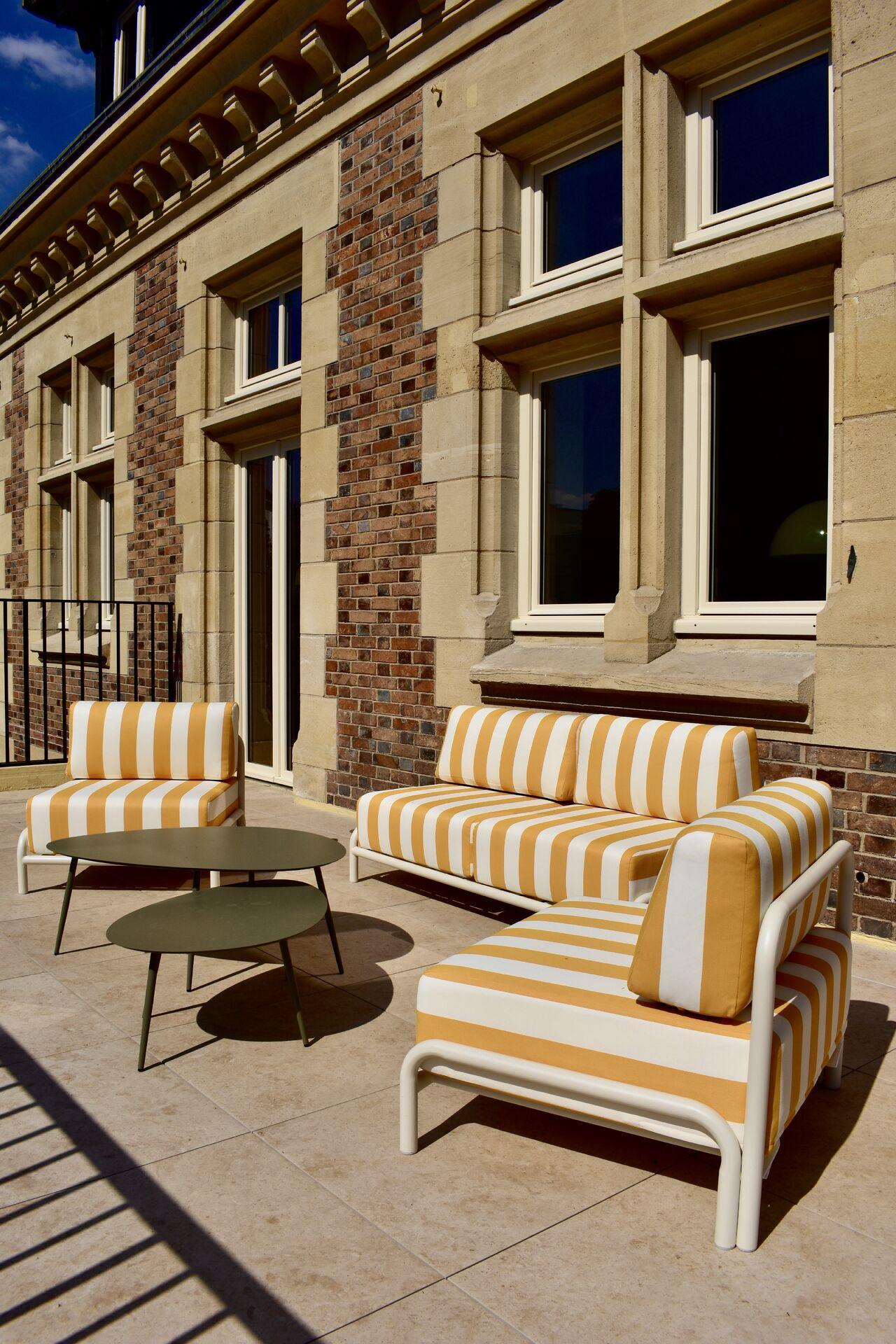 Outdoor terrace at Le Grand Comet, with yellow striped sofas along the stone façade