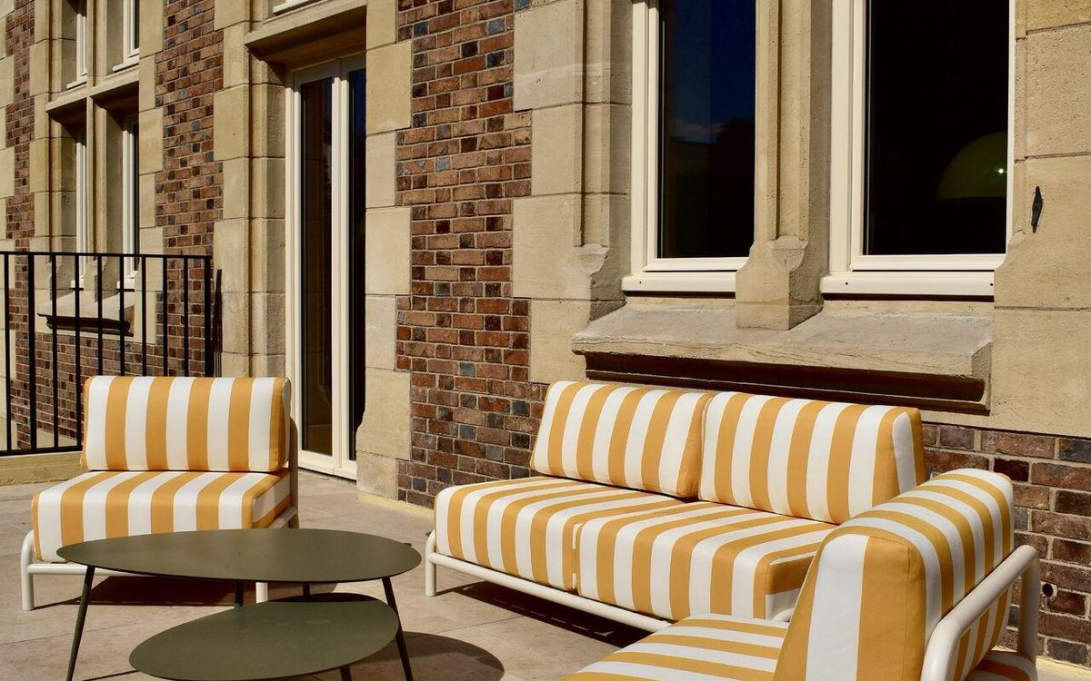 Outdoor terrace at Le Grand Comet, with yellow striped sofas along the stone façade
