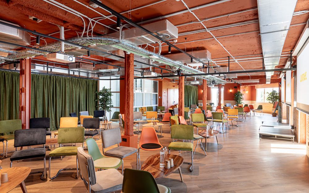 Un étage en configuration cabaret, avec rideaux de velours vert, poteaux orange et petite scène au fond.