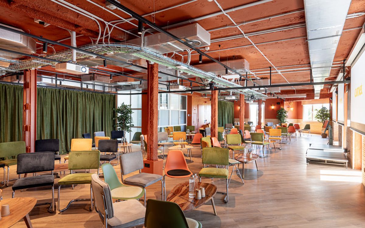 Una planta en configuración cabaré, con cortinas de terciopelo verde, pilares naranjas y un pequeño escenario al fondo.
