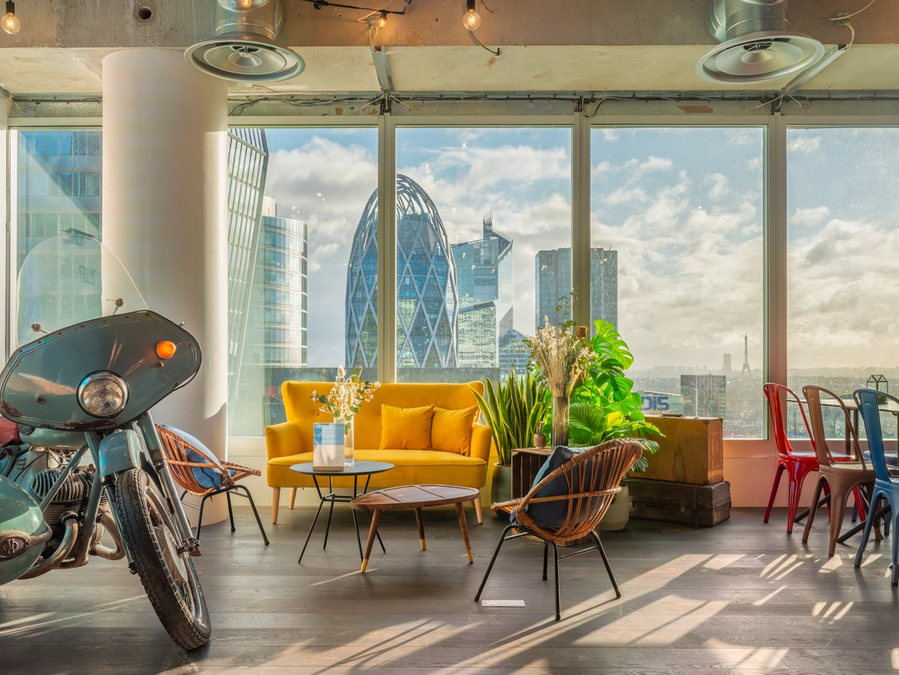 Salon de Comet Cœur Défense avec son canapé jaune, sa moto vintage et la vue sur les tours de la Défense