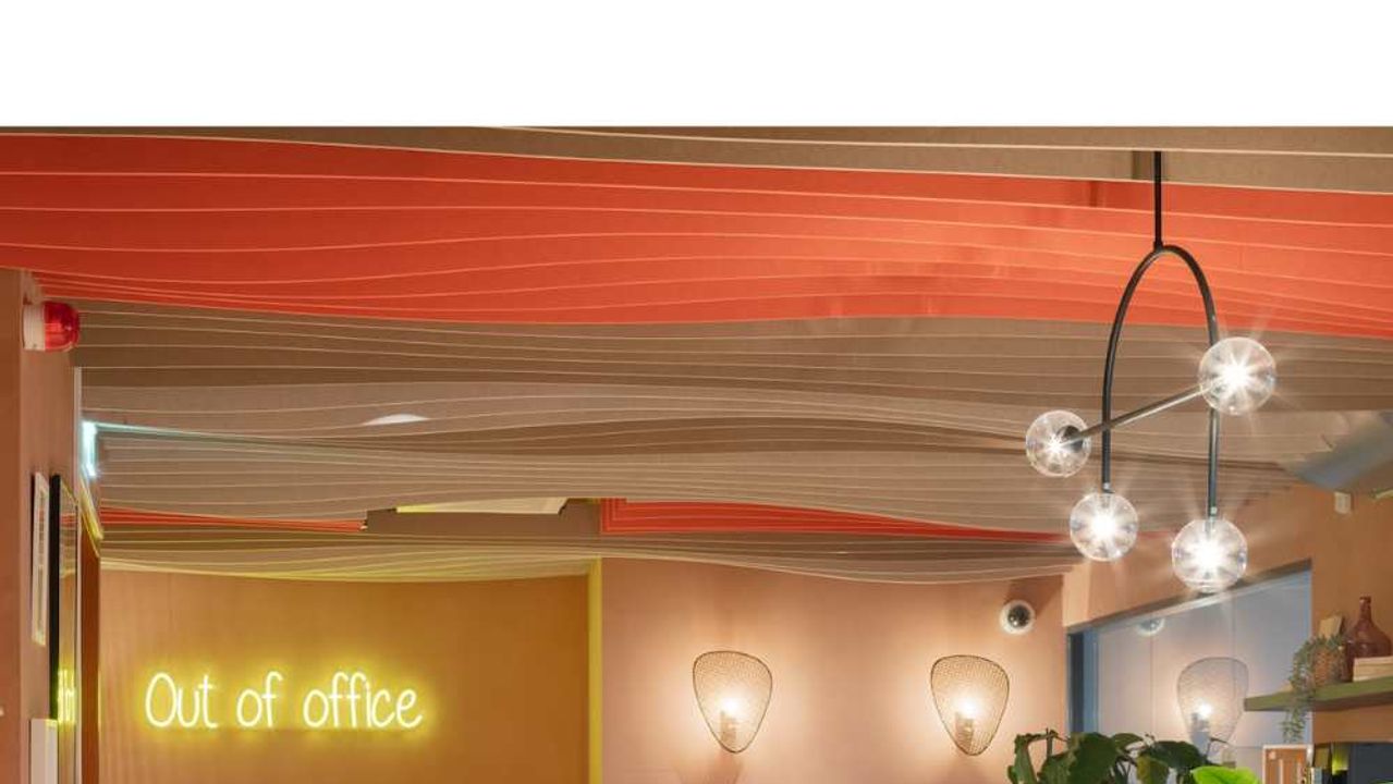 Ontvangstruimte in oranje tinten, met een plafond van golvende stoffen banen en een neonbord « Out of office » aan de muur.
