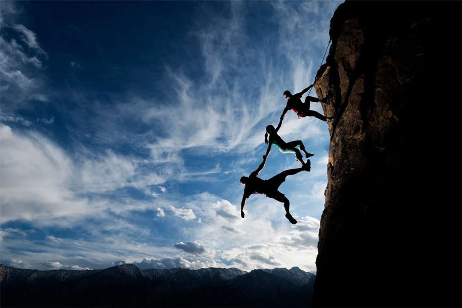 CLimbers relying on trust by holding on to each other whilst scaling a cliff face.