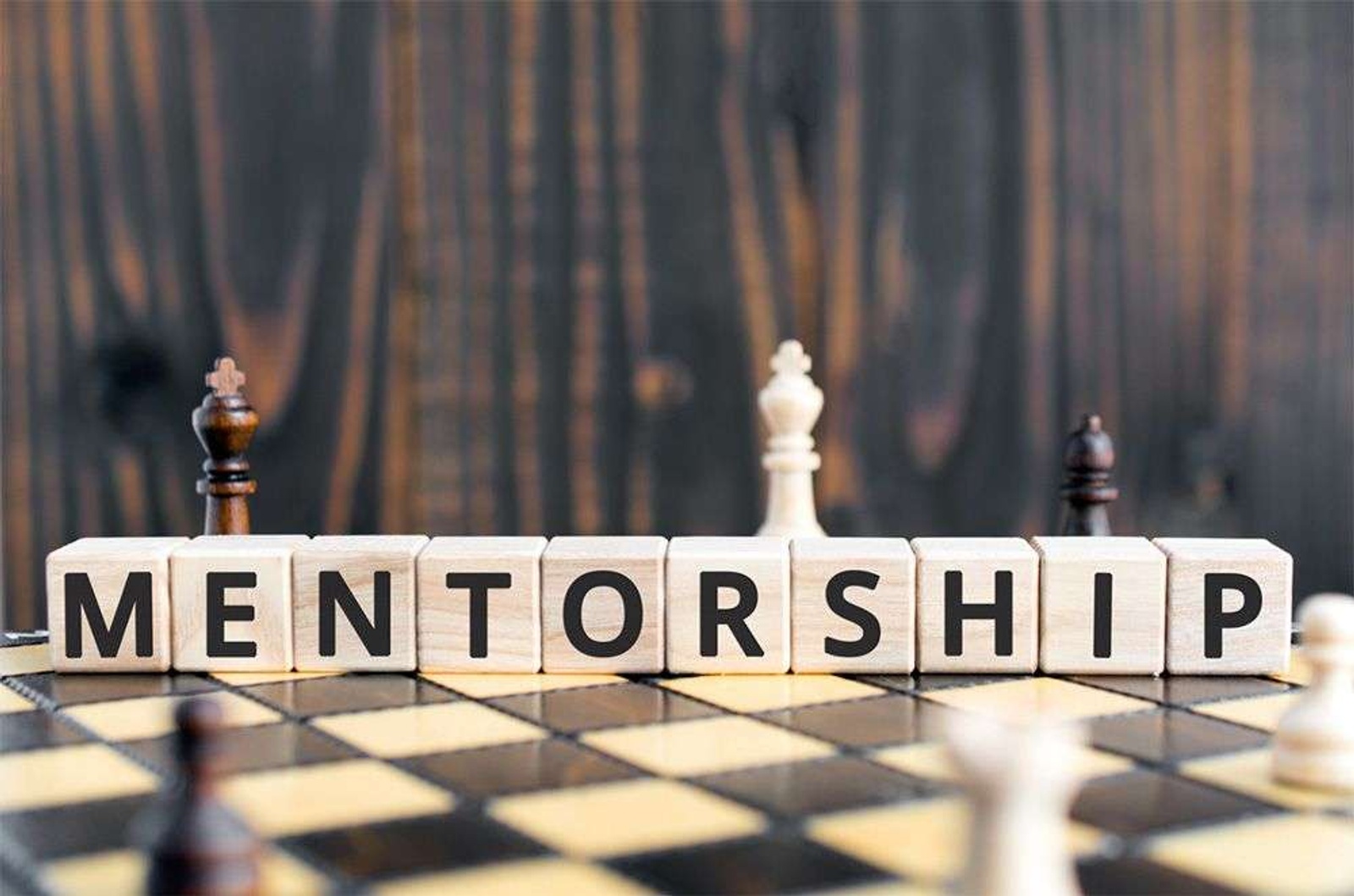 Mentorship spelled out in blocks over a chess board.