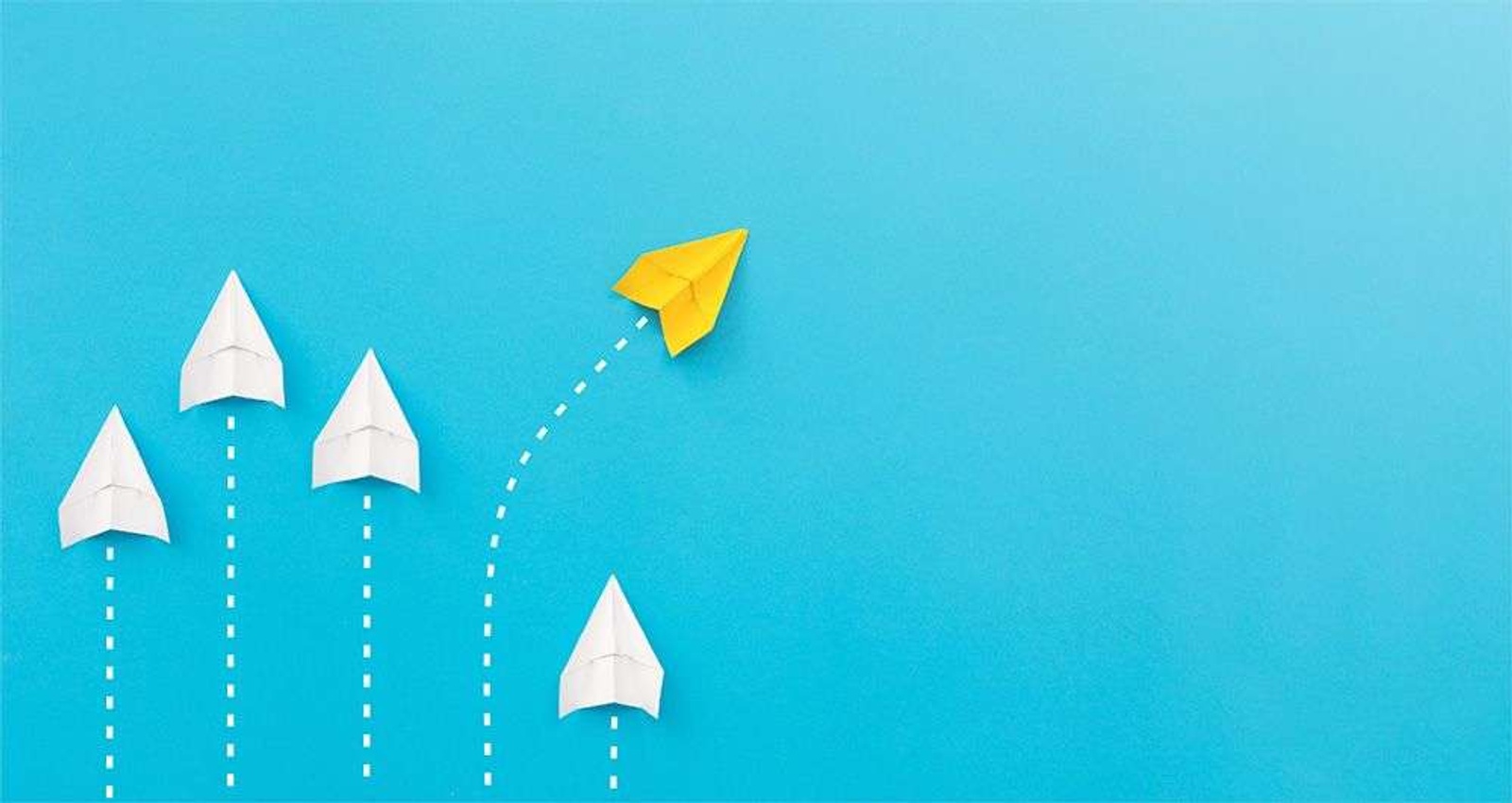 A yellow paper aeroplane breaks away from a group of white paper aeroplanes.