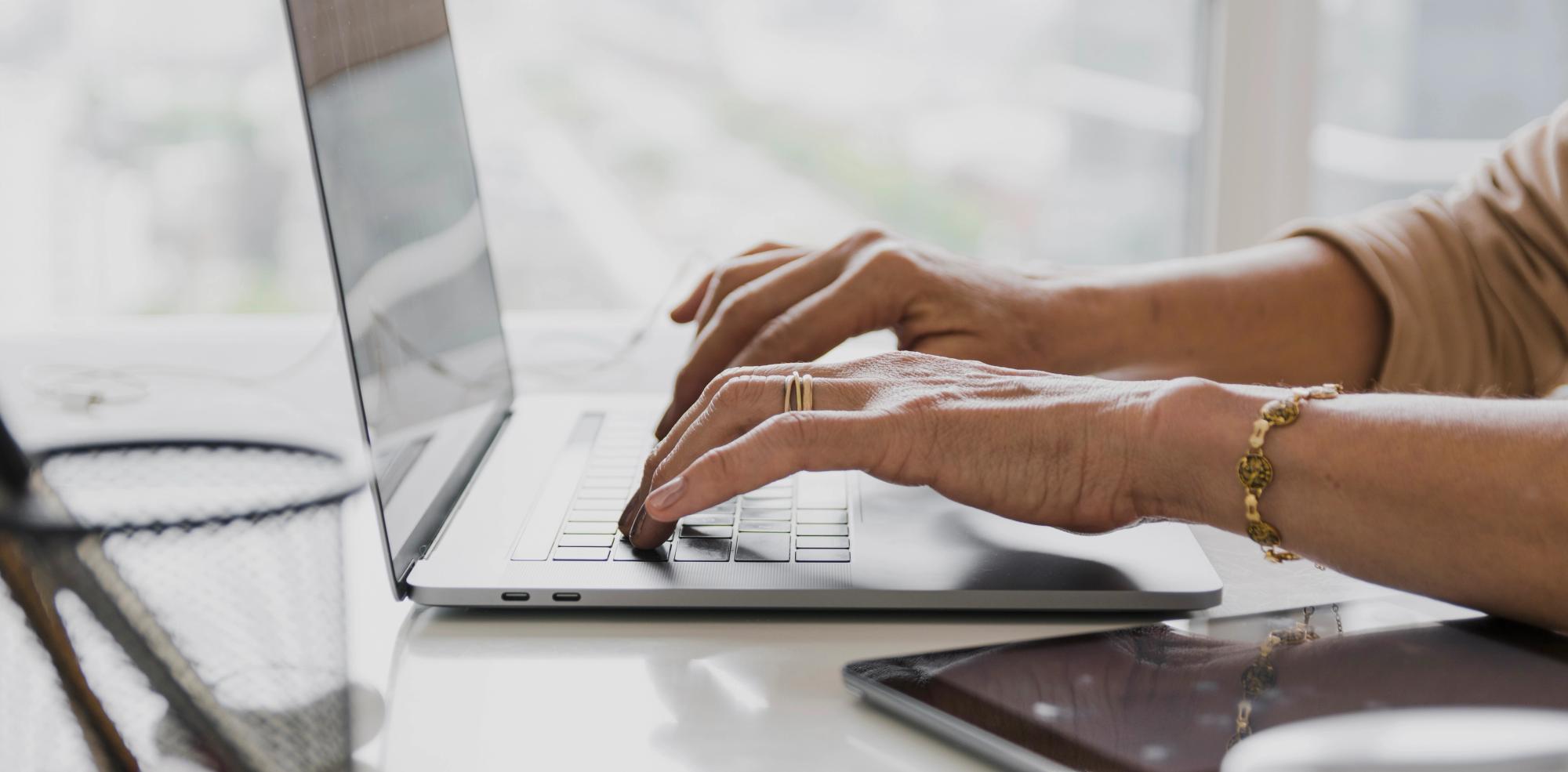 Hands typing a follow-up email after meeting on a laptop, drafting next steps and action items in a post-meeting recap email.