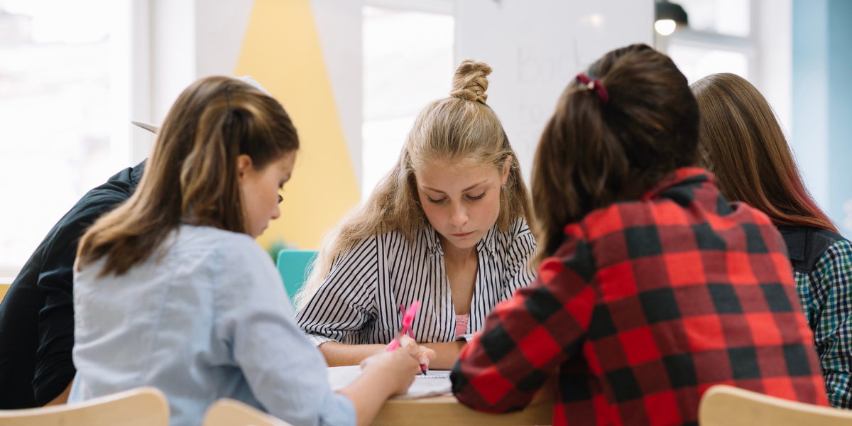 chicas adolescentes sentadas alrededor de una mesa redonda para fortalecer habilidades de trabajo en equipo