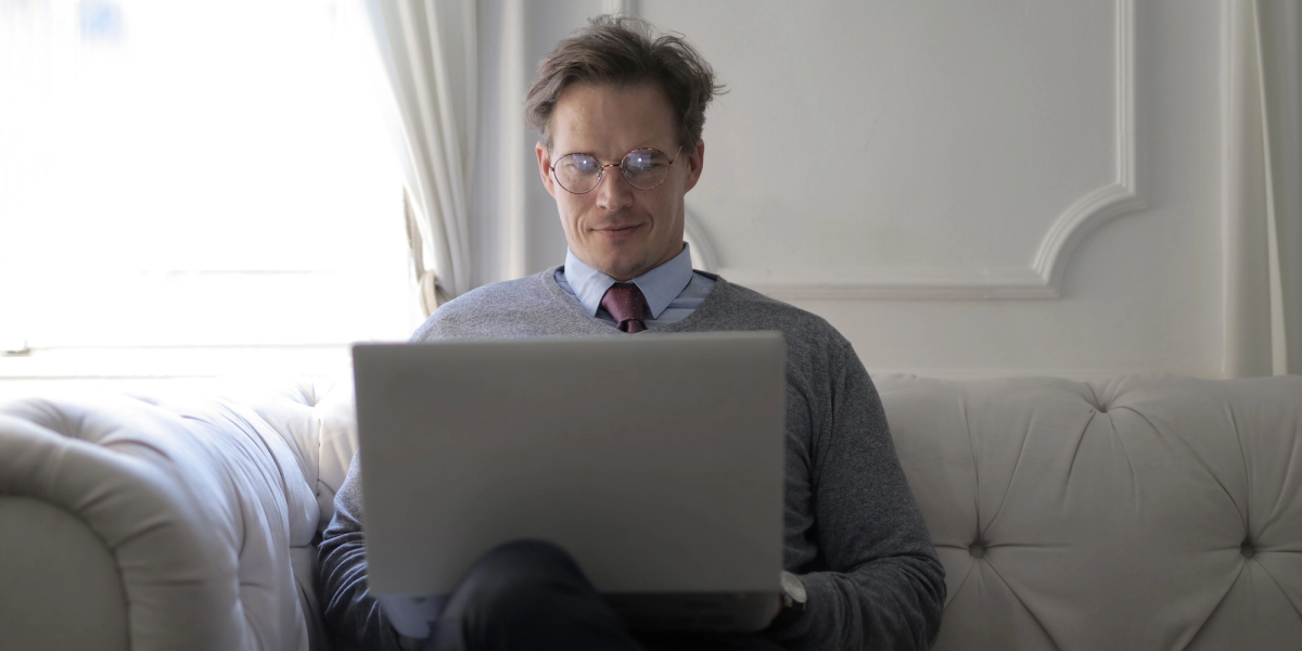 man with glasses sitting on a couch with a laptop checking how to create a poll in outlook