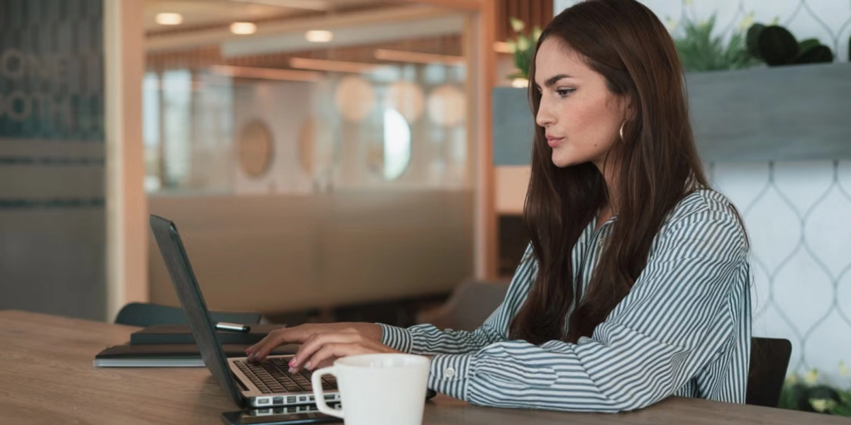 woman in a striped shirt working by a computer in an office and not knowing how to ask someone for their availability for a meeting 