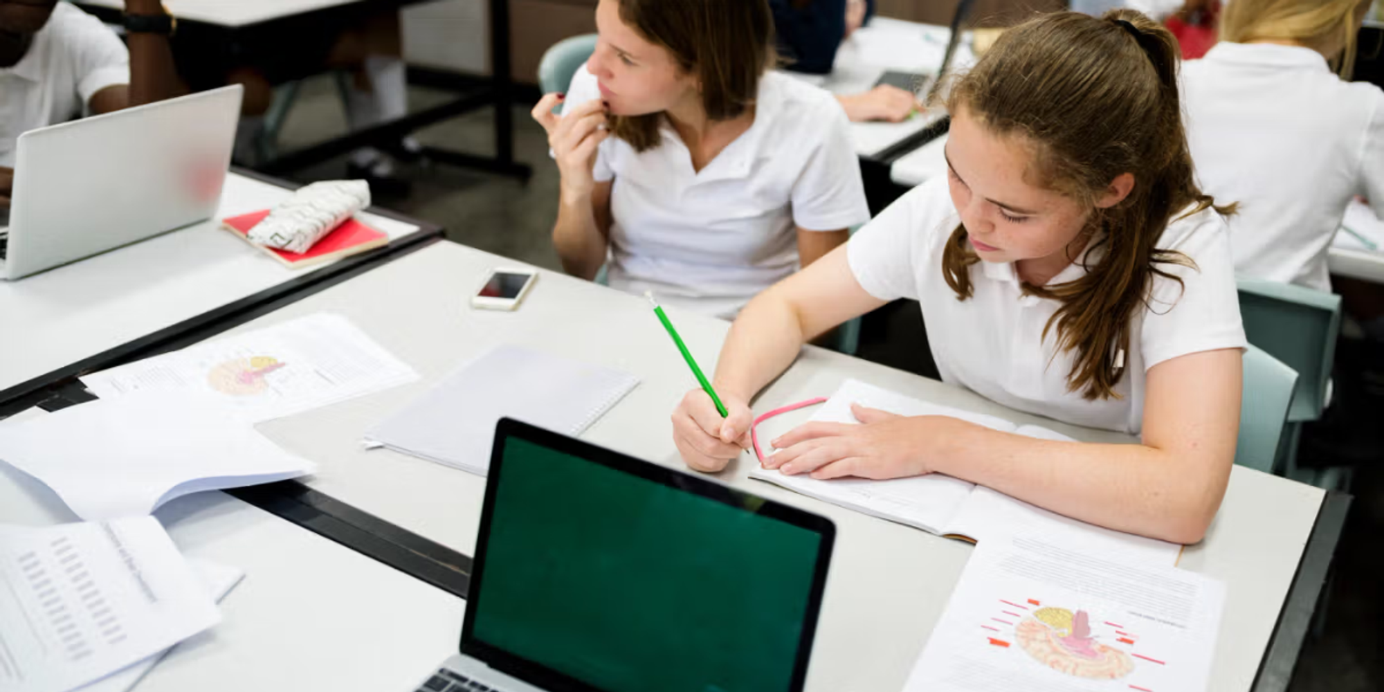 Pupils working with laptops and notes in class, highlighting the value of a student information system for schools.