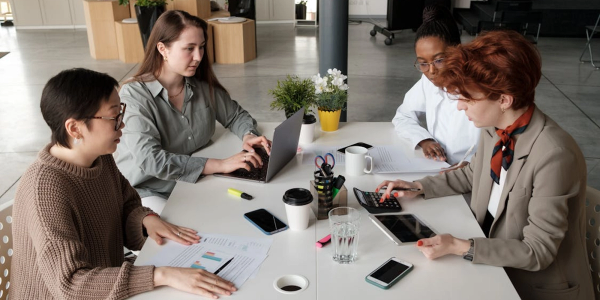 four women from an accounting team sitting by a table discussing zoho books pricing  