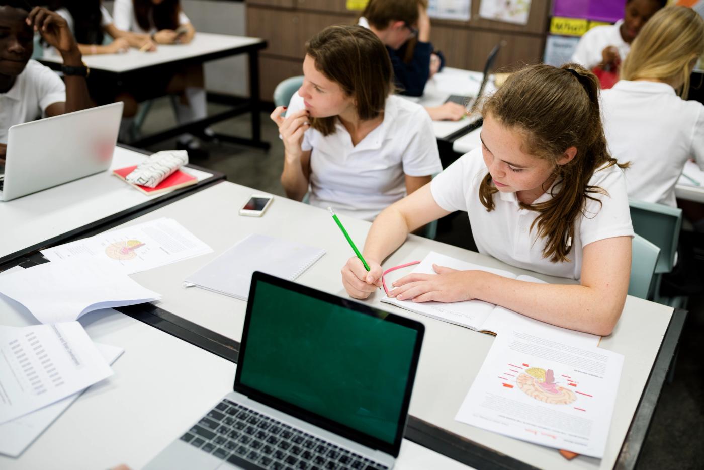 Pupils working with laptops and notes in class, highlighting the value of a student information system for schools.