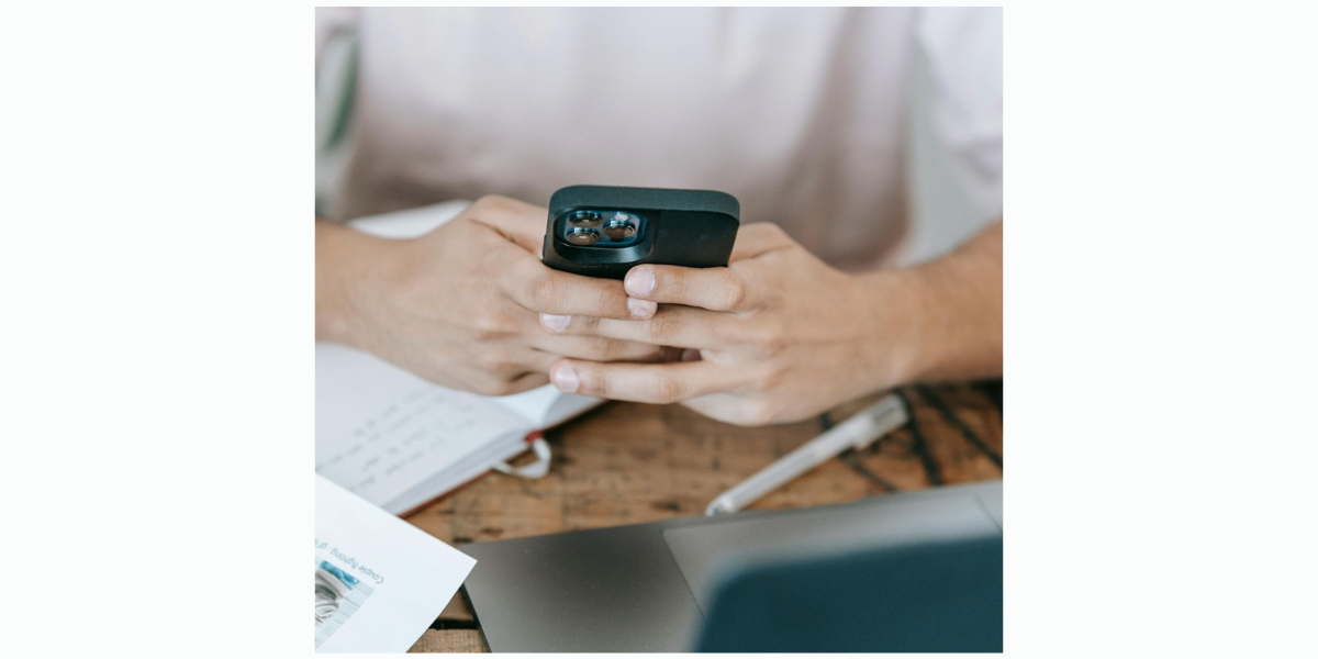 Close-up of someone on their phone at a desk scheduling SMS reminders with Google Calendar