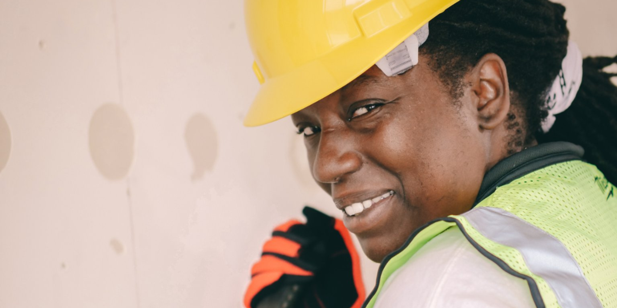 Smiling electrician wearing a yellow hard hat and safety vest while working indoors