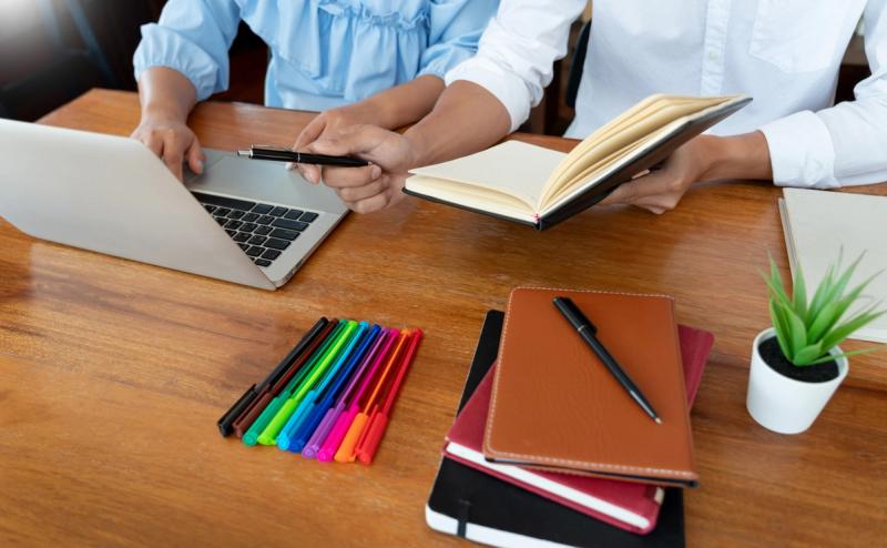 Teachers collaborating on laptop using a school administration software setup at a shared workspace.