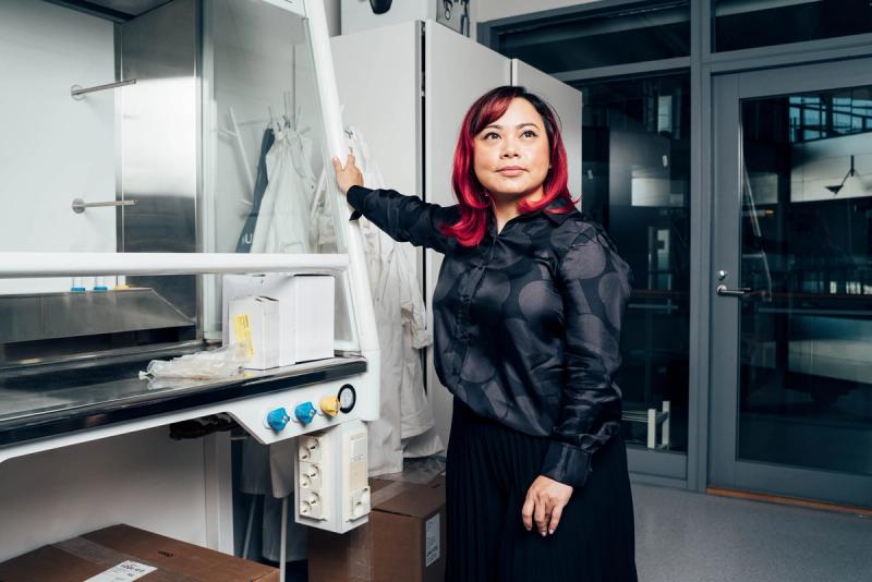 Windi Muziasari standing in her lab, a large piece of lab equipment, looking thoughtfully into the distance.