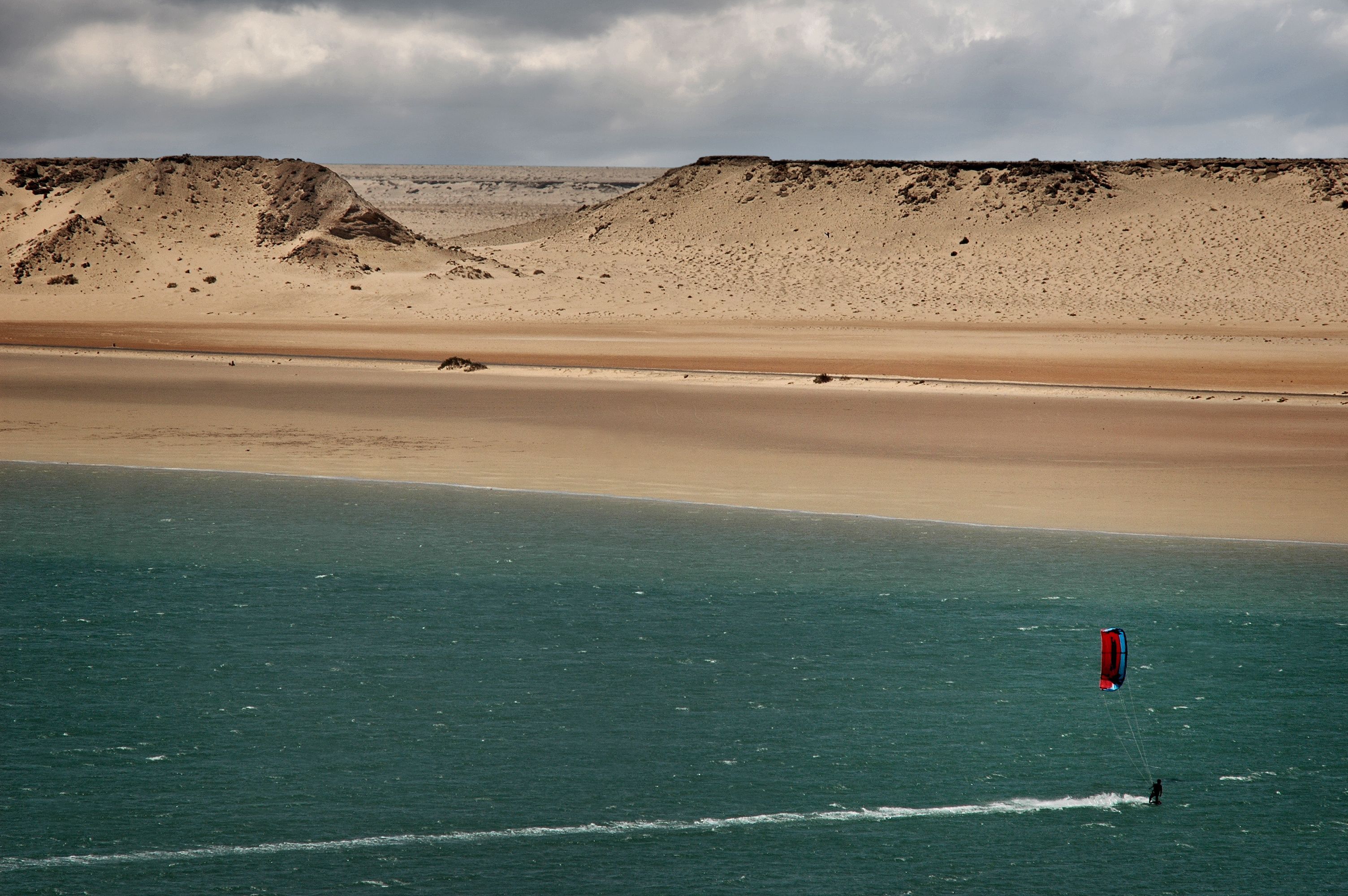A kitesurfer crossing the Dakhla lagoon below pale dunes