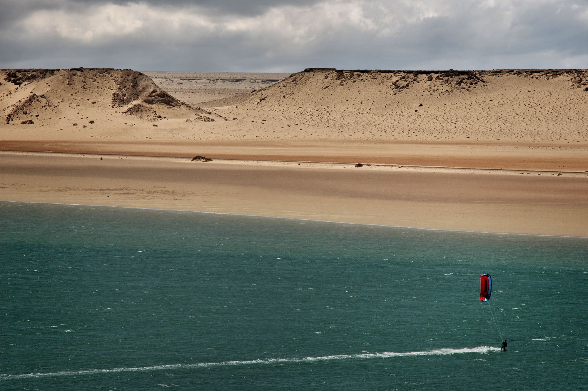A kitesurfer crossing the Dakhla lagoon below pale dunes