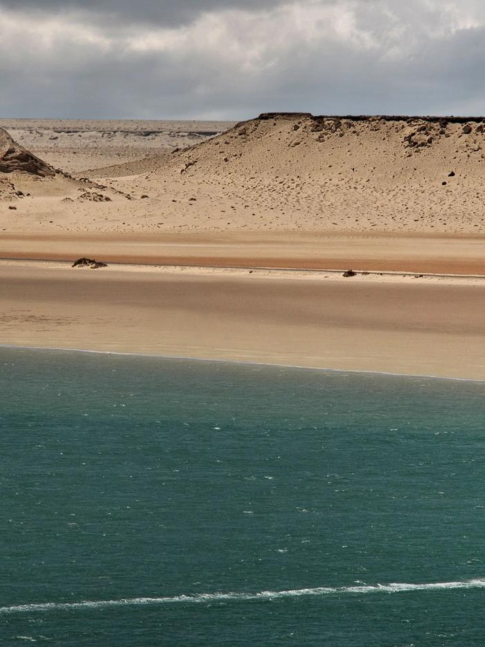 A kitesurfer crossing the Dakhla lagoon below pale dunes