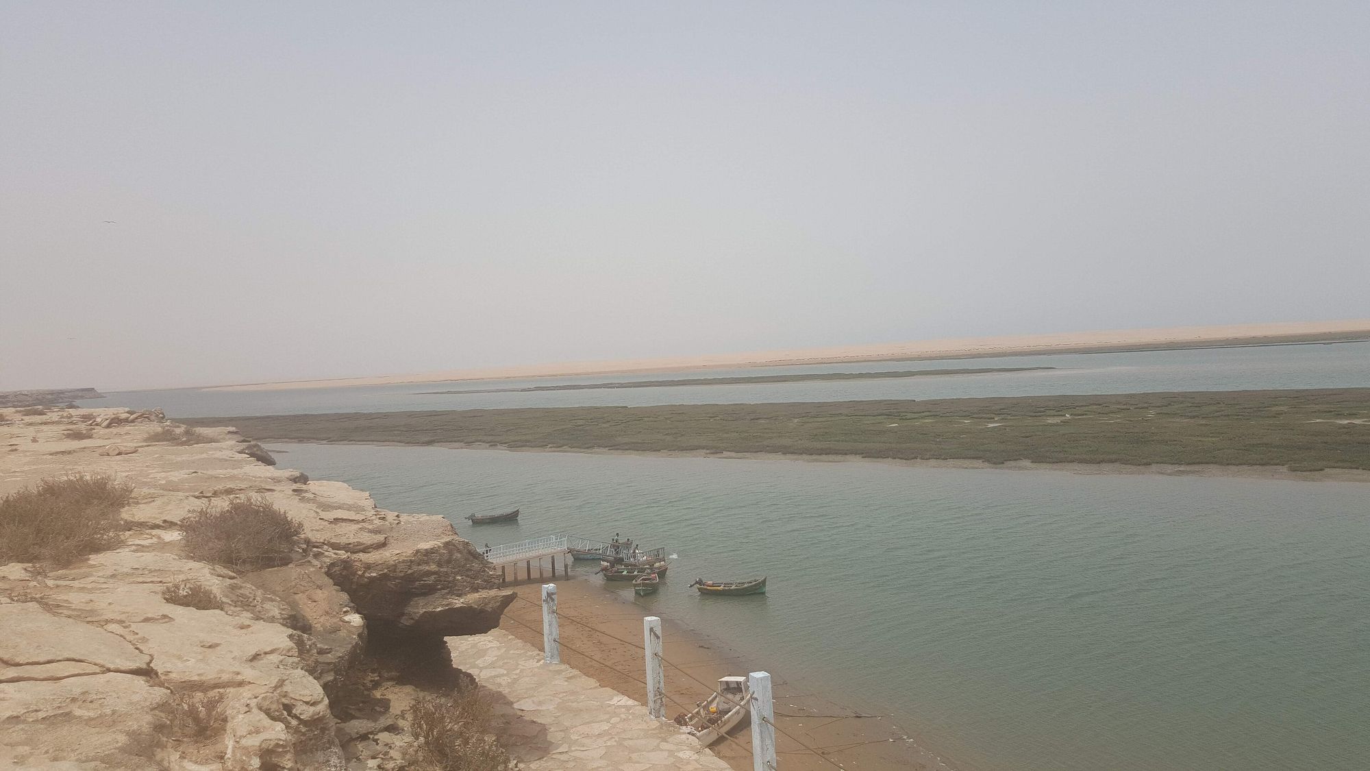 Fishing boats moored in the Khnifiss Lagoon below a low limestone cliff