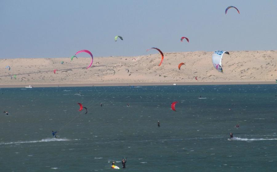 Dozens of kites over the Dakhla lagoon, with pale dunes on the far shore