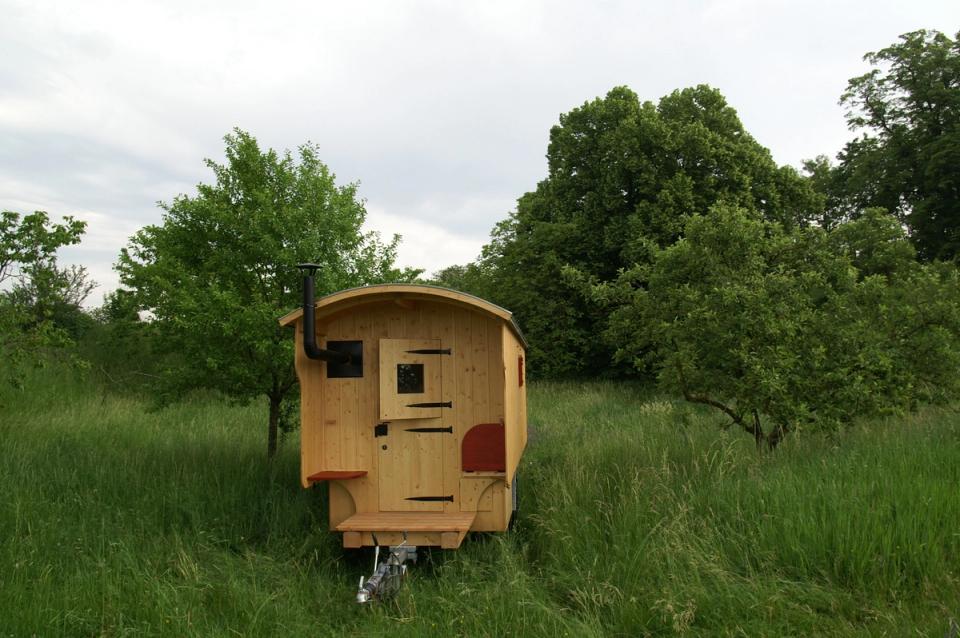 Schäferwagen aus hellem Holz mit rotem Fensterladen in einer Streuobstwiese