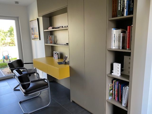 Büro mit olivfarbenen Einbauschränken und gelbem Schreibtisch