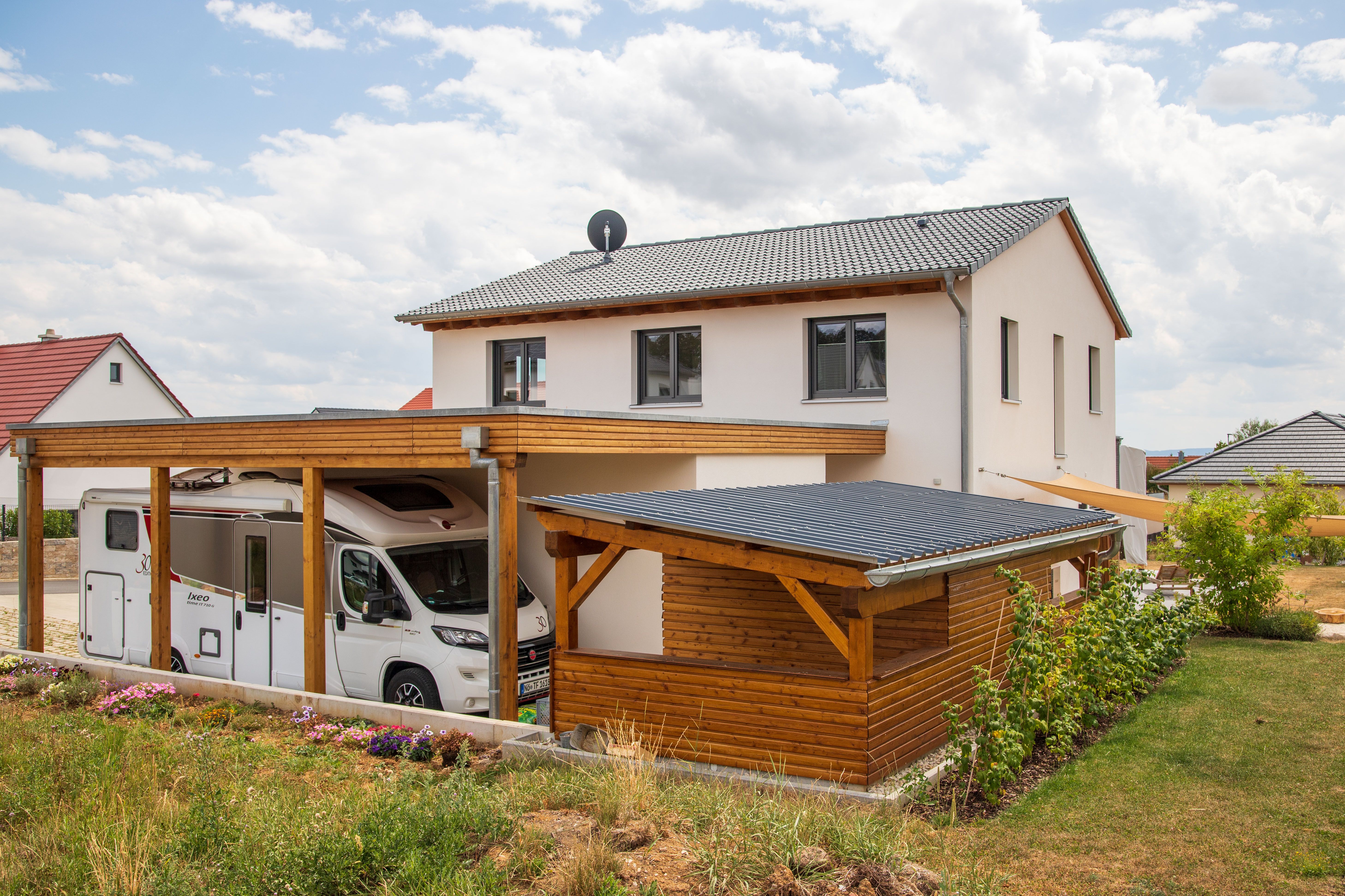 Neubau mit Satteldach, Carport und Holzgartenhaus im Sommer