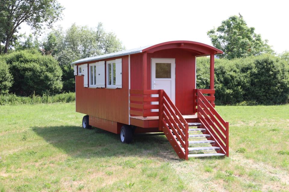 Roter Waldkindergartenwagen mit überdachtem Eingang und breiter Treppe auf einer Wiese