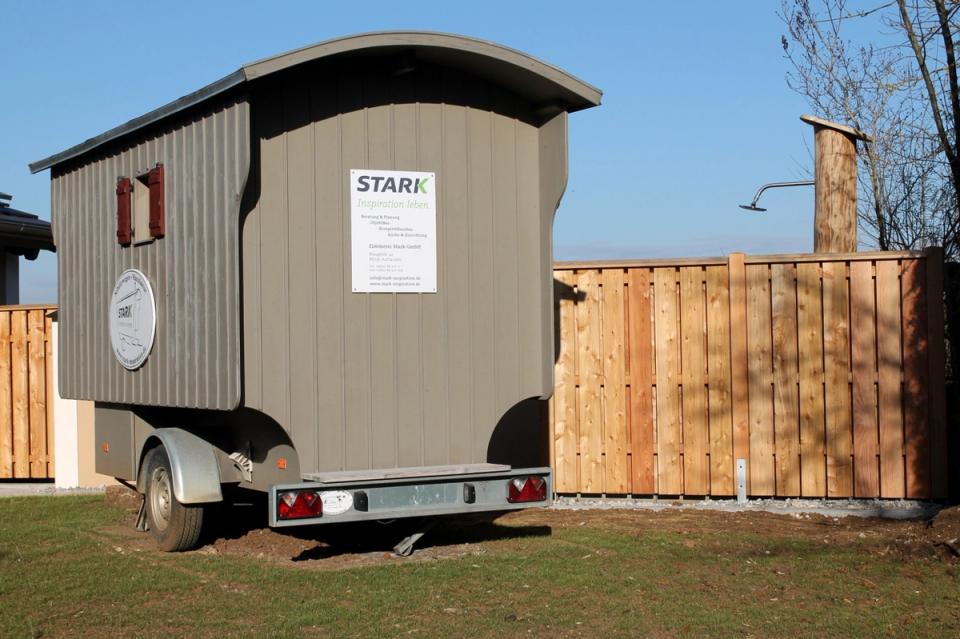 Schäferwagen-Sauna mit STARK-Schild hinter dem Holzzaun