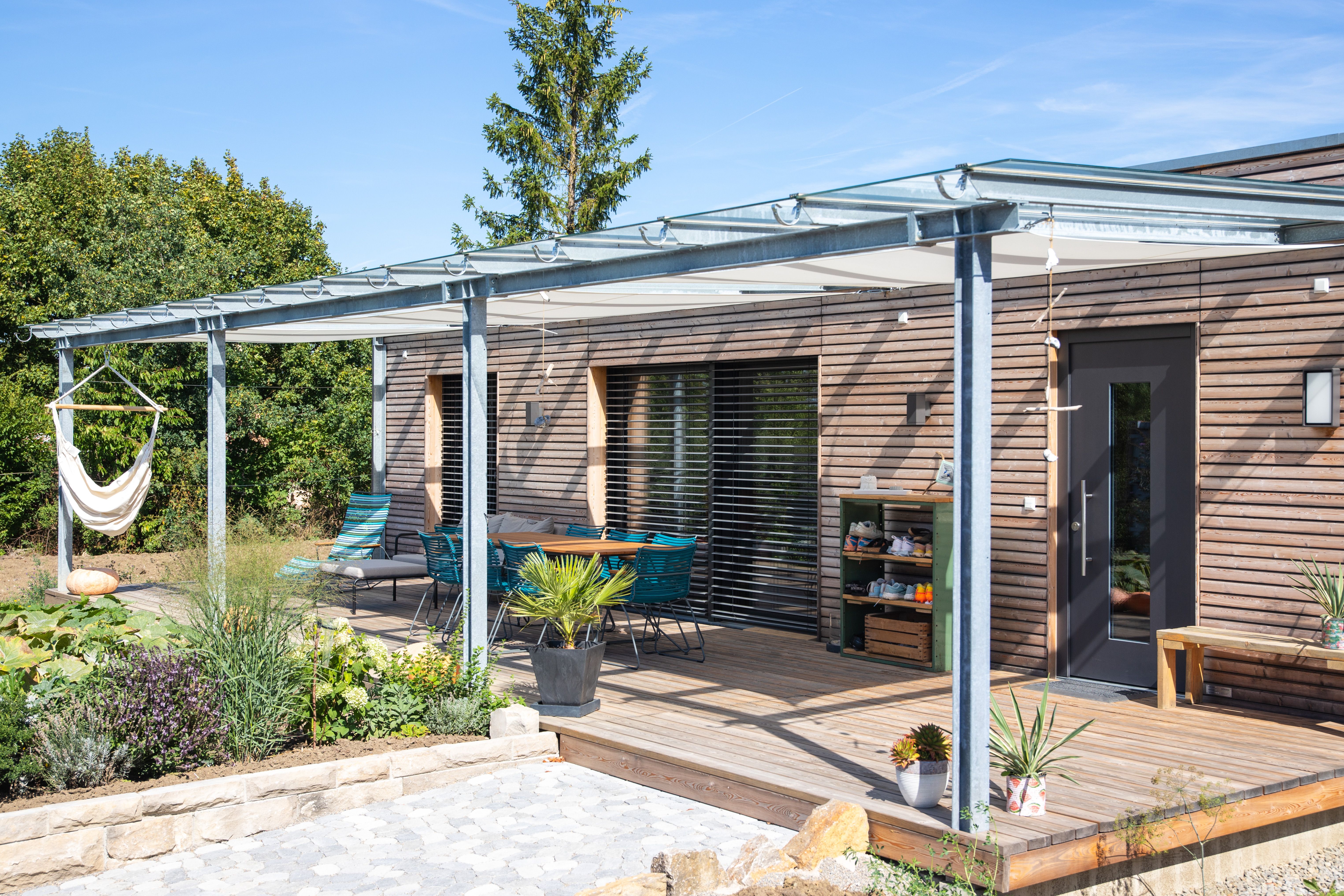 Holzterrasse mit Stahl-Glas-Pergola, Hängesessel und Gartenbeeten