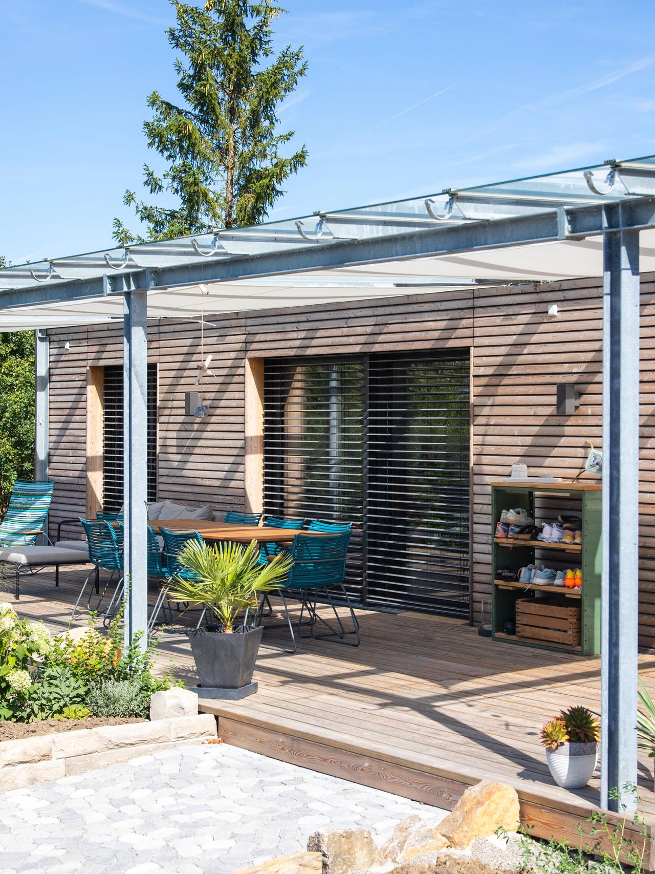 Holzterrasse mit Stahl-Glas-Pergola, Hängesessel und Gartenbeeten