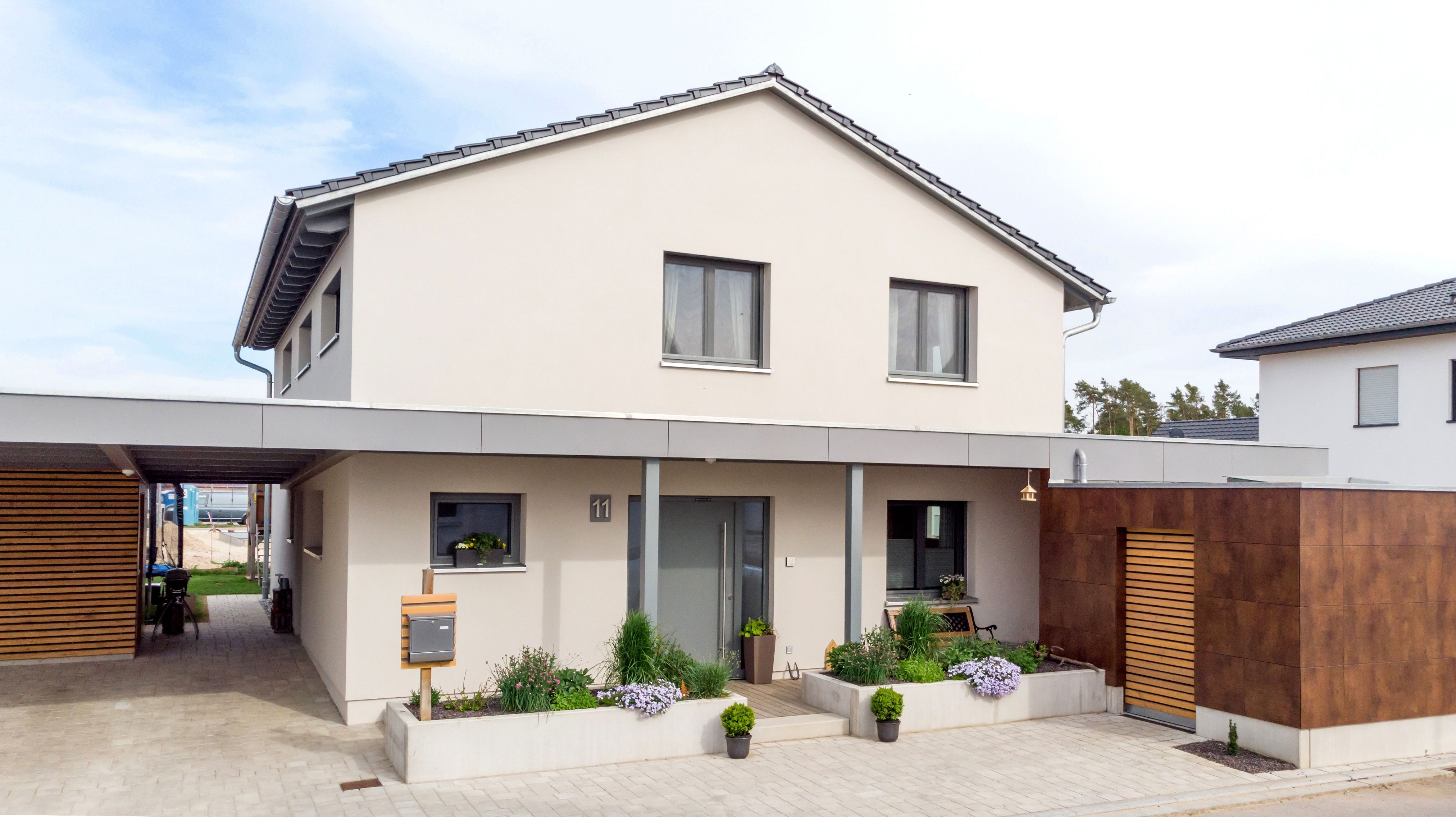 Hausfront mit Satteldach, Eingangsvordach und Carport bei blauem Himmel