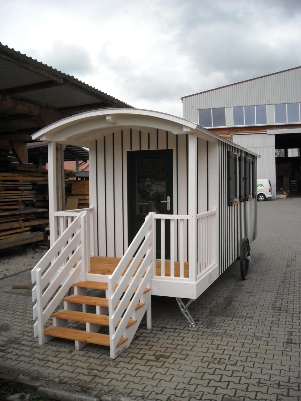 Weißer Zirkuswagen von vorn: Veranda mit gewölbtem Dach, Geländer und Treppe