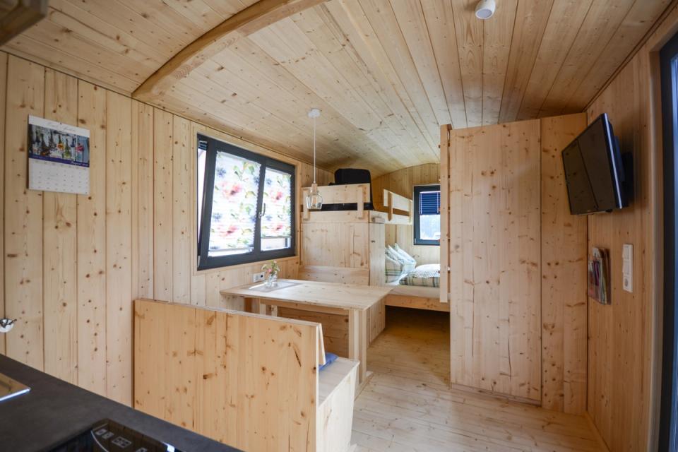 Innenraum eines Ferienwagens mit Tisch, Doppelbett im hinteren Teil und Fernseher an der Wand