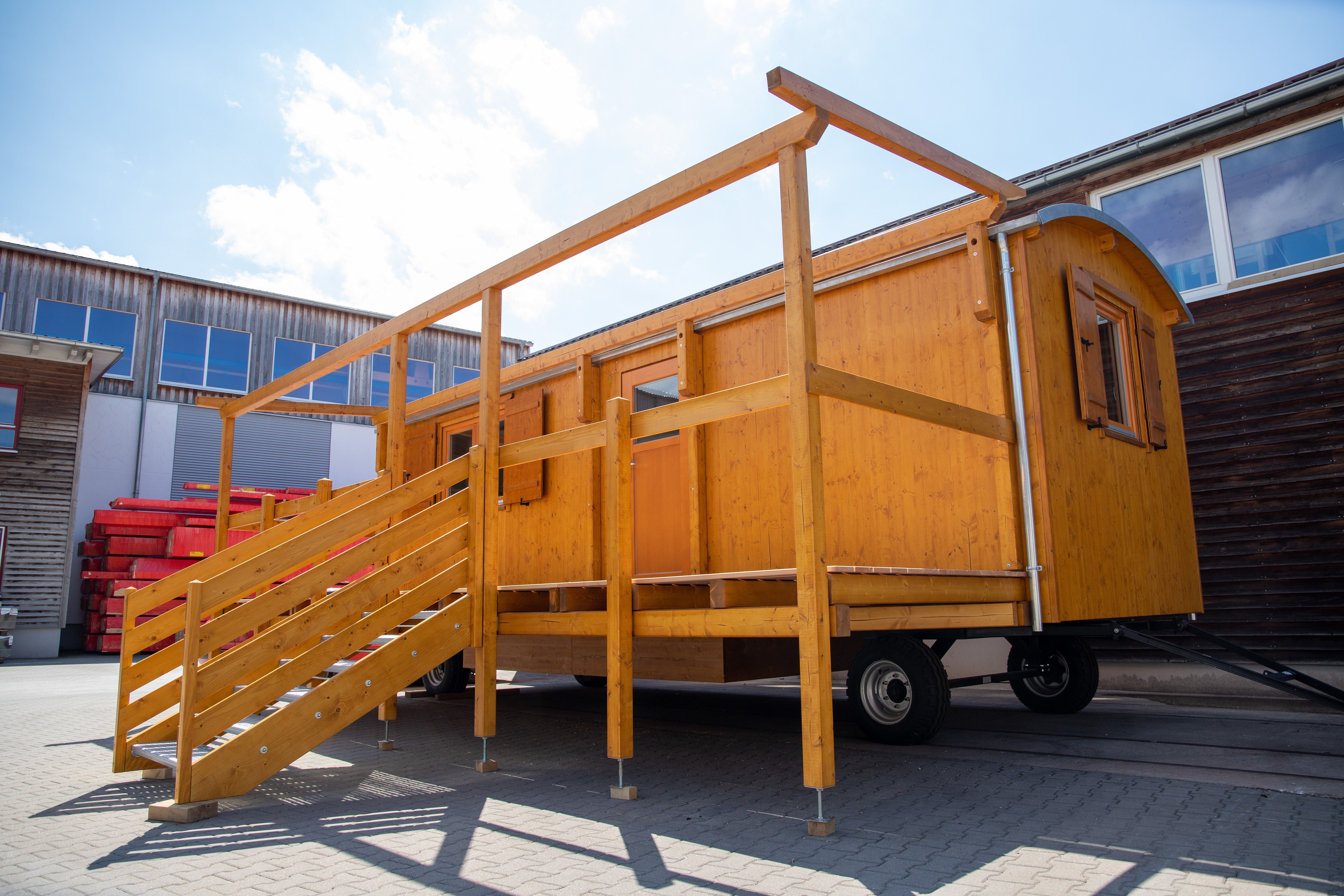Honigfarbener Waldkindergartenwagen von der Seite: Terrasse mit Treppe und Geländer, darüber das Gerüst für ein Sonnendach