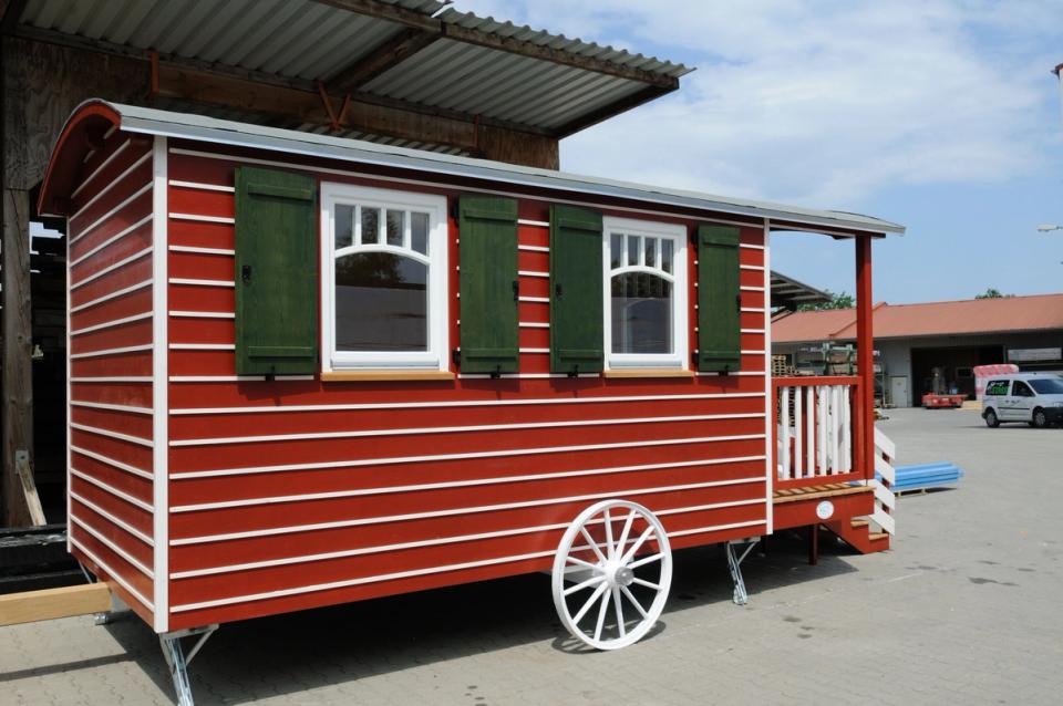 Rot-weiß gestreifter Zirkuswagen von der Seite mit Sprossenfenstern und grünen Fensterläden