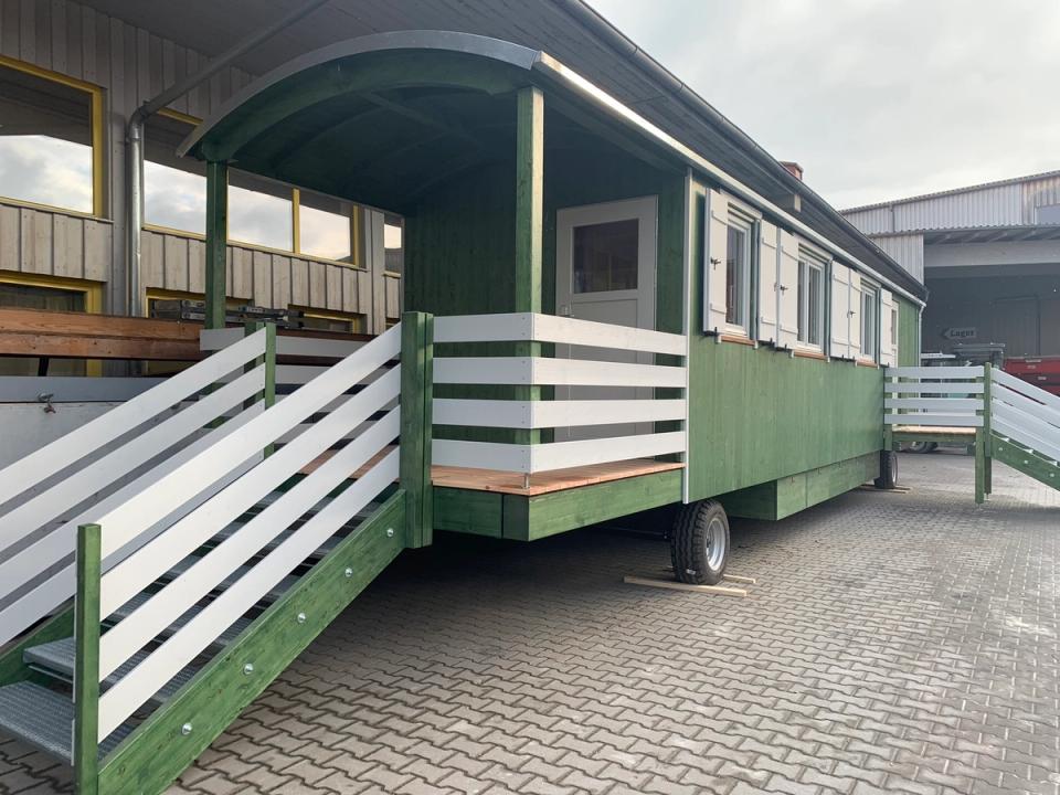 Überdachter Eingang mit weißem Geländer und Stahltreppe an einem grünen Waldkindergartenwagen