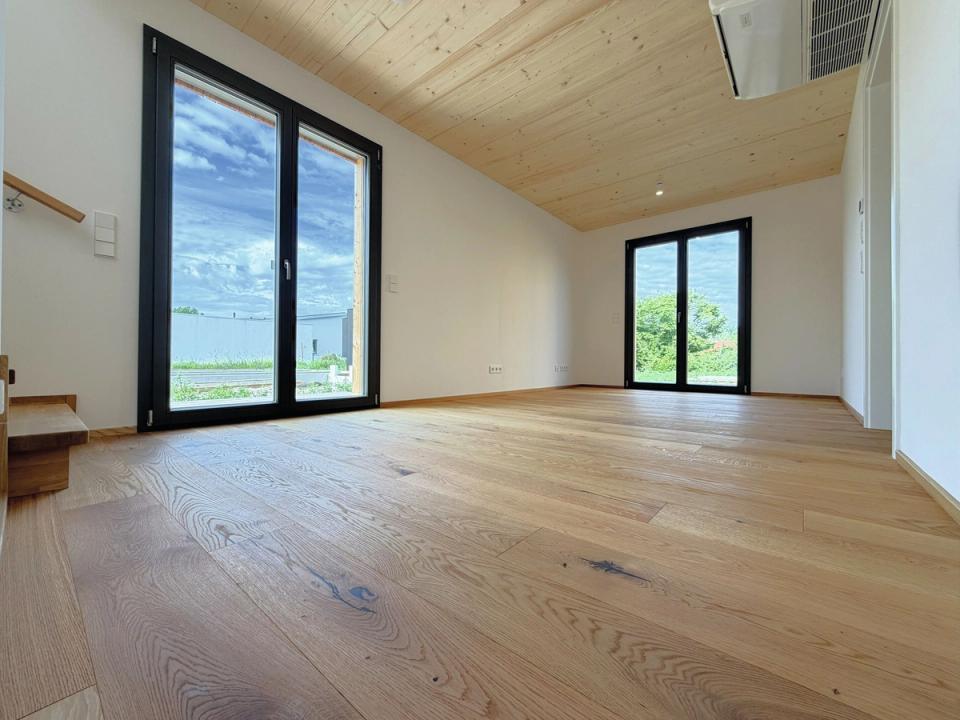 Heller Wohnraum mit bodentiefen Fenstern, Holzdecke und Eichenparkett