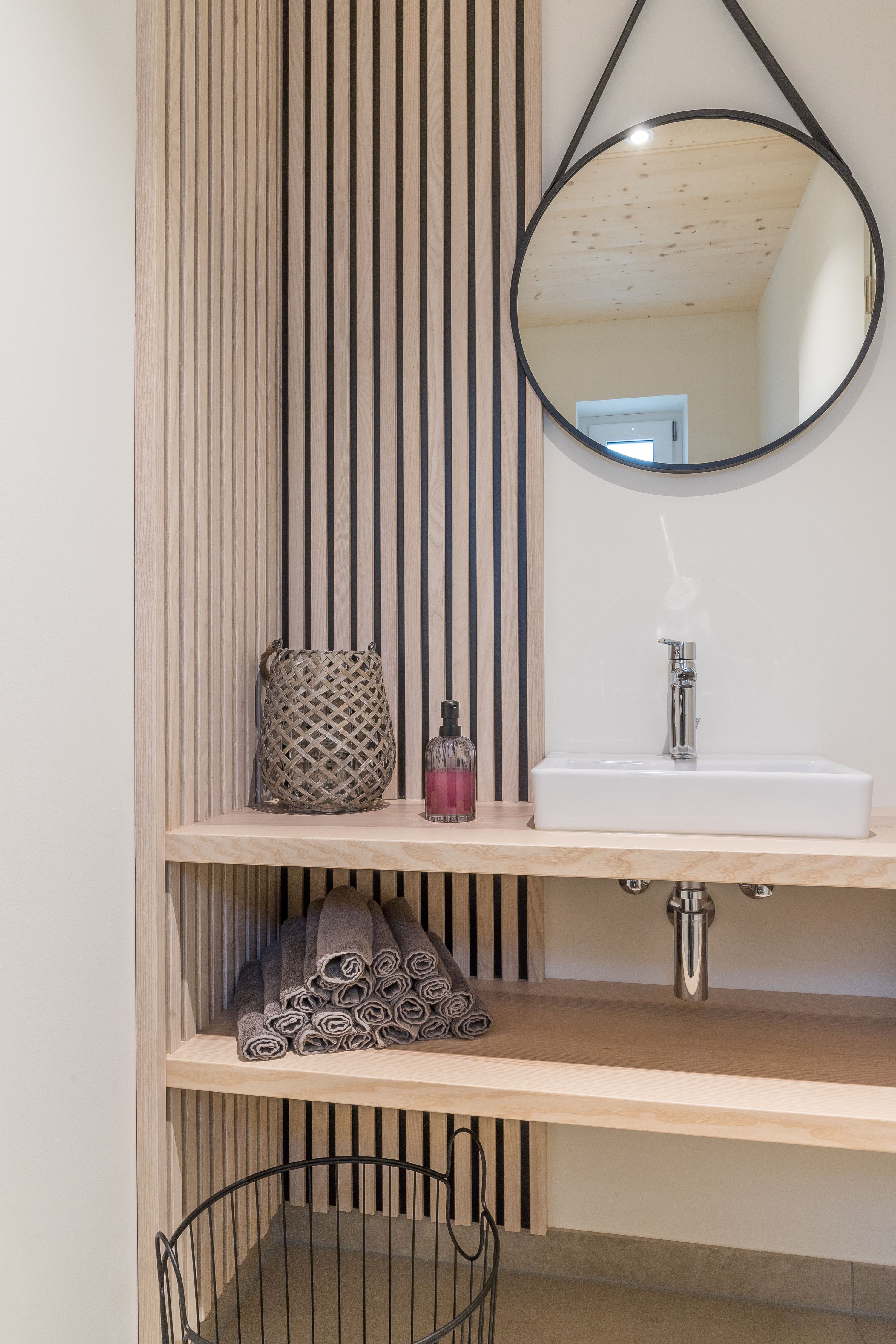 Gäste-WC mit Holzlamellenwand, rundem Spiegel und Aufsatzwaschbecken