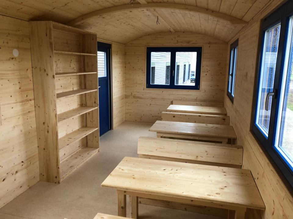 Innenraum mit niedrigen Tischen und Bänken für Kinder, Bücherregal und dunklen Fensterrahmen