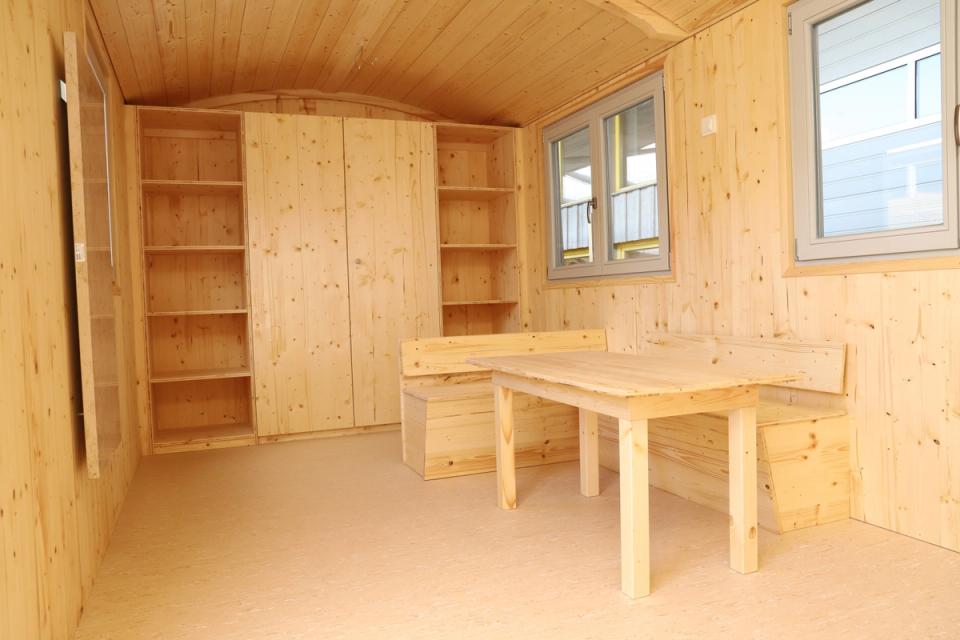 Innenraum aus hellem Fichtenholz mit Eckbank, Tisch, offenen Regalen und Einbauschrank