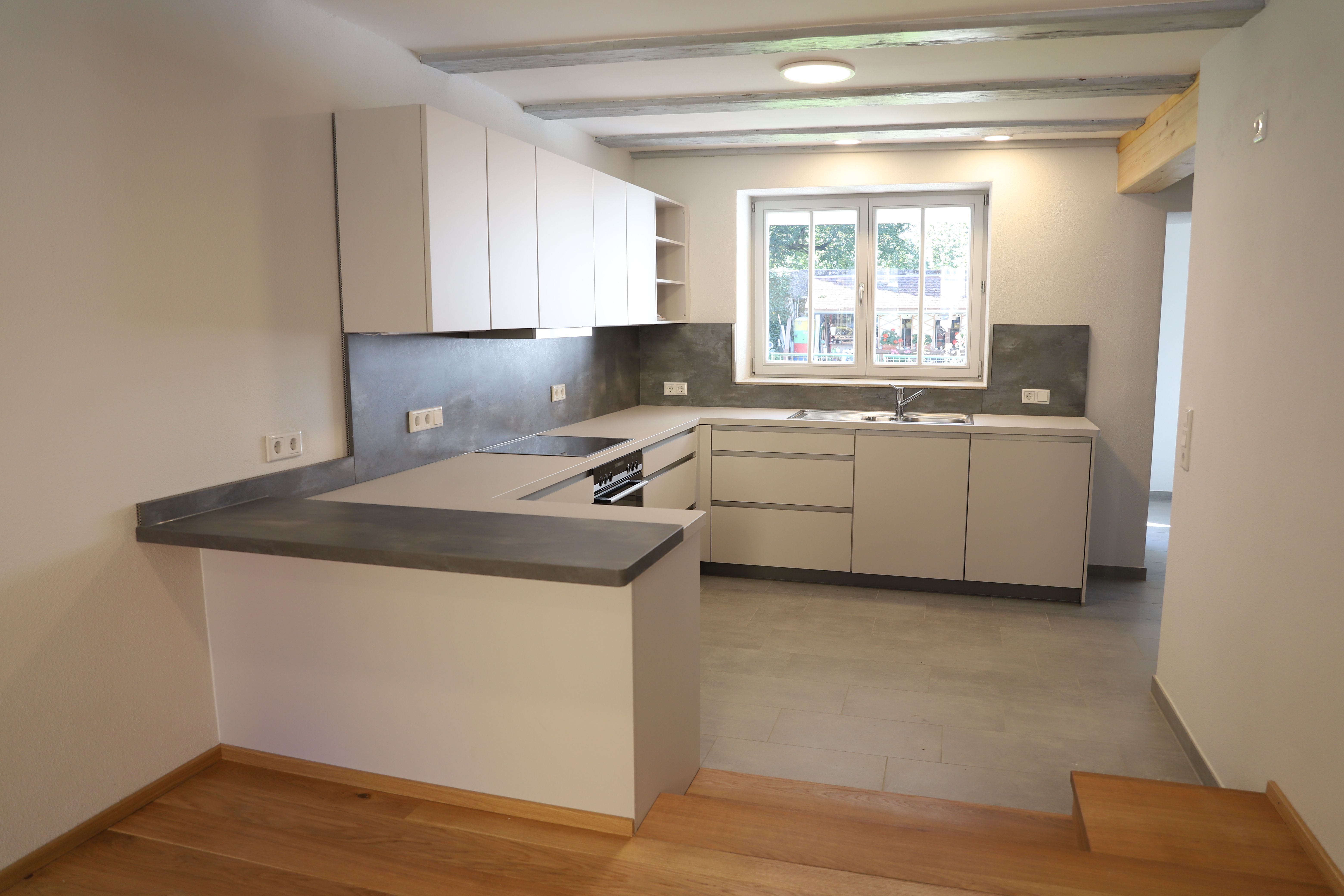 Moderne Küche mit weißen Fronten, grauer Rückwand und Sprossenfenster