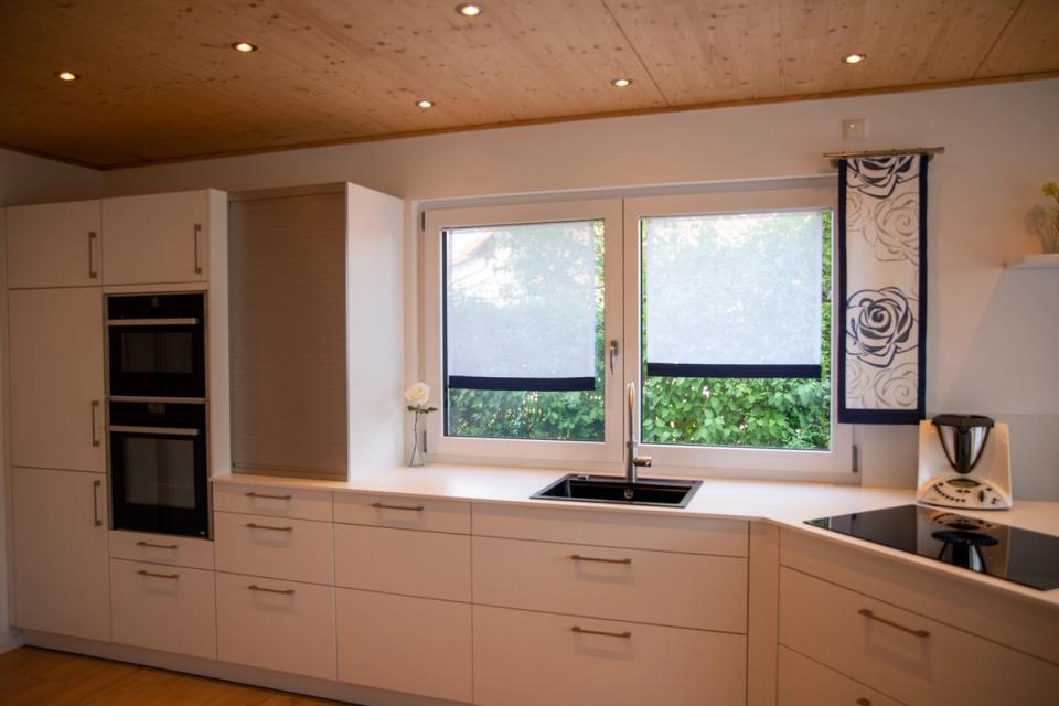 Weiße Einbauküche mit Holzdecke, Eckfenster und schwarzer Spüle