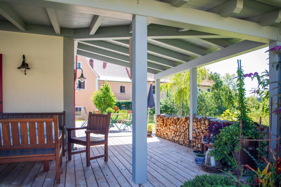Überdachte Terrasse mit Holzbänken, Brennholz und Gartenblick
