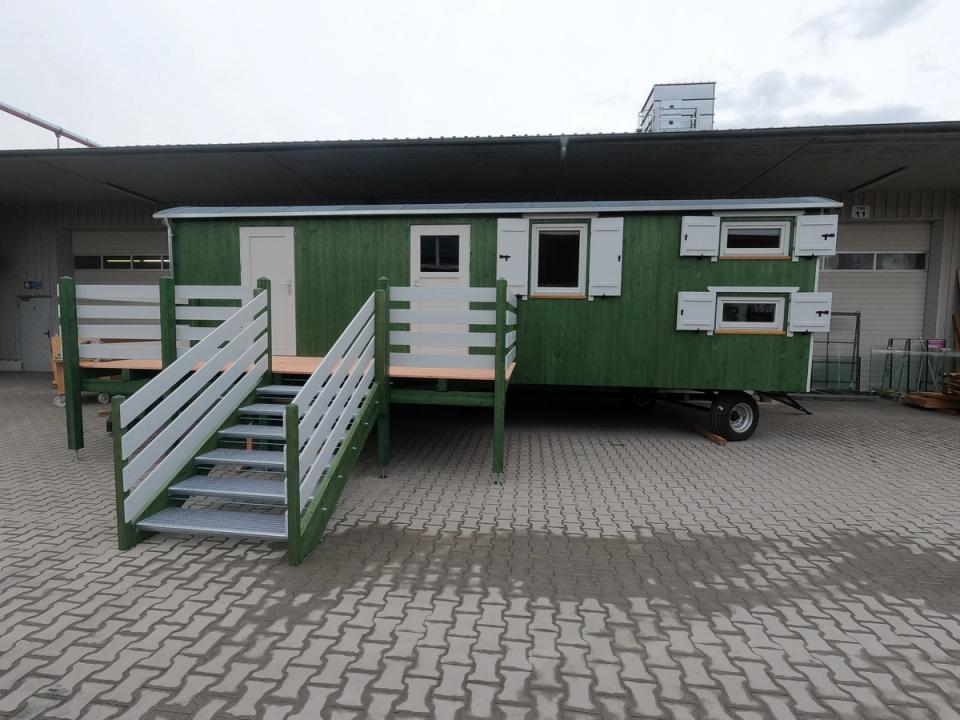 Grüner Waldkindergartenwagen mit Podest, weißem Geländer und zwei Treppen vor der Halle der Zimmerei