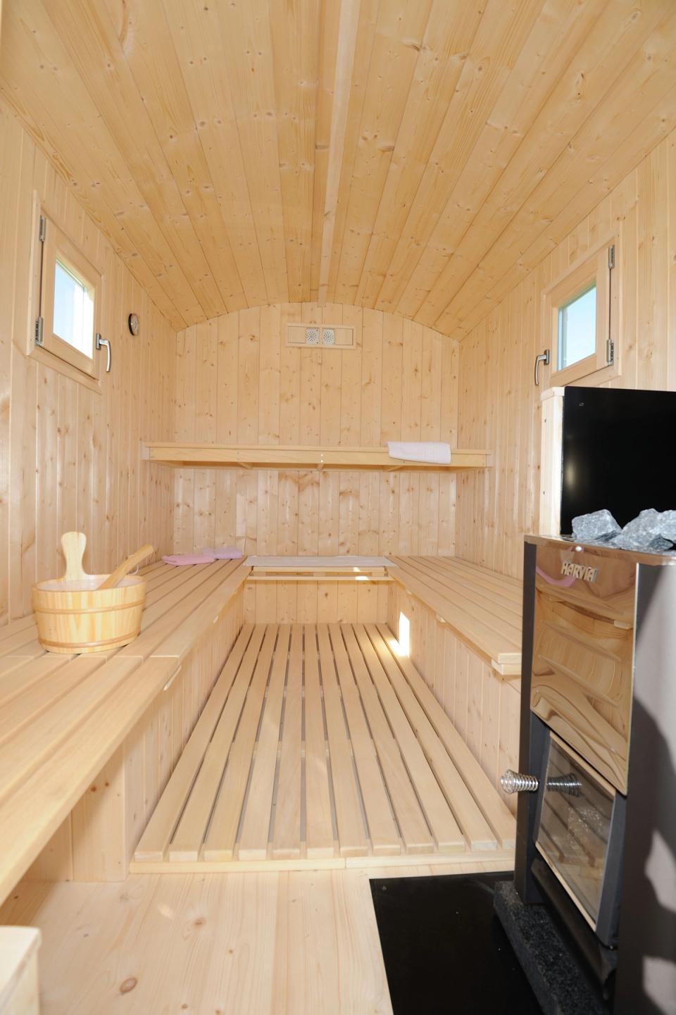 Saunabänke aus hellem Holz auf zwei Ebenen, rechts der Saunaofen